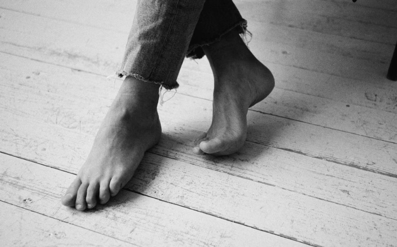 Bare feet on floorboards beside a bed in dim light