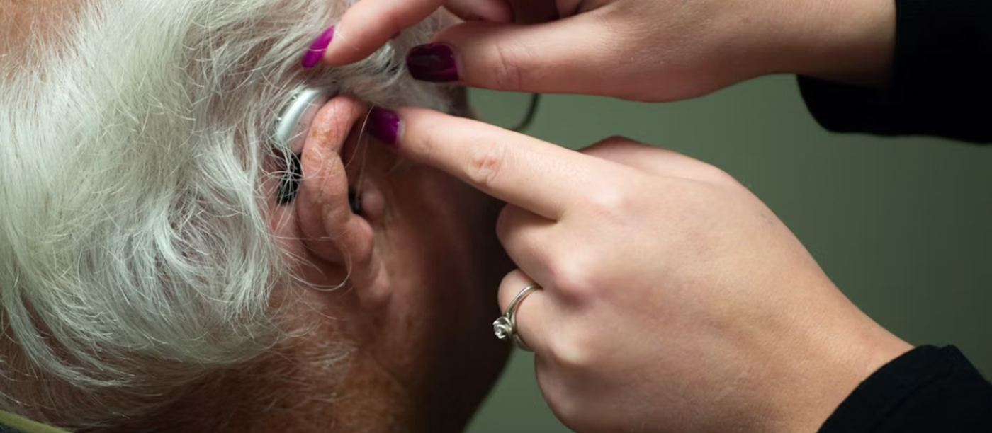 An audiologist fitting a behind-the-ear hearing aid for an older man