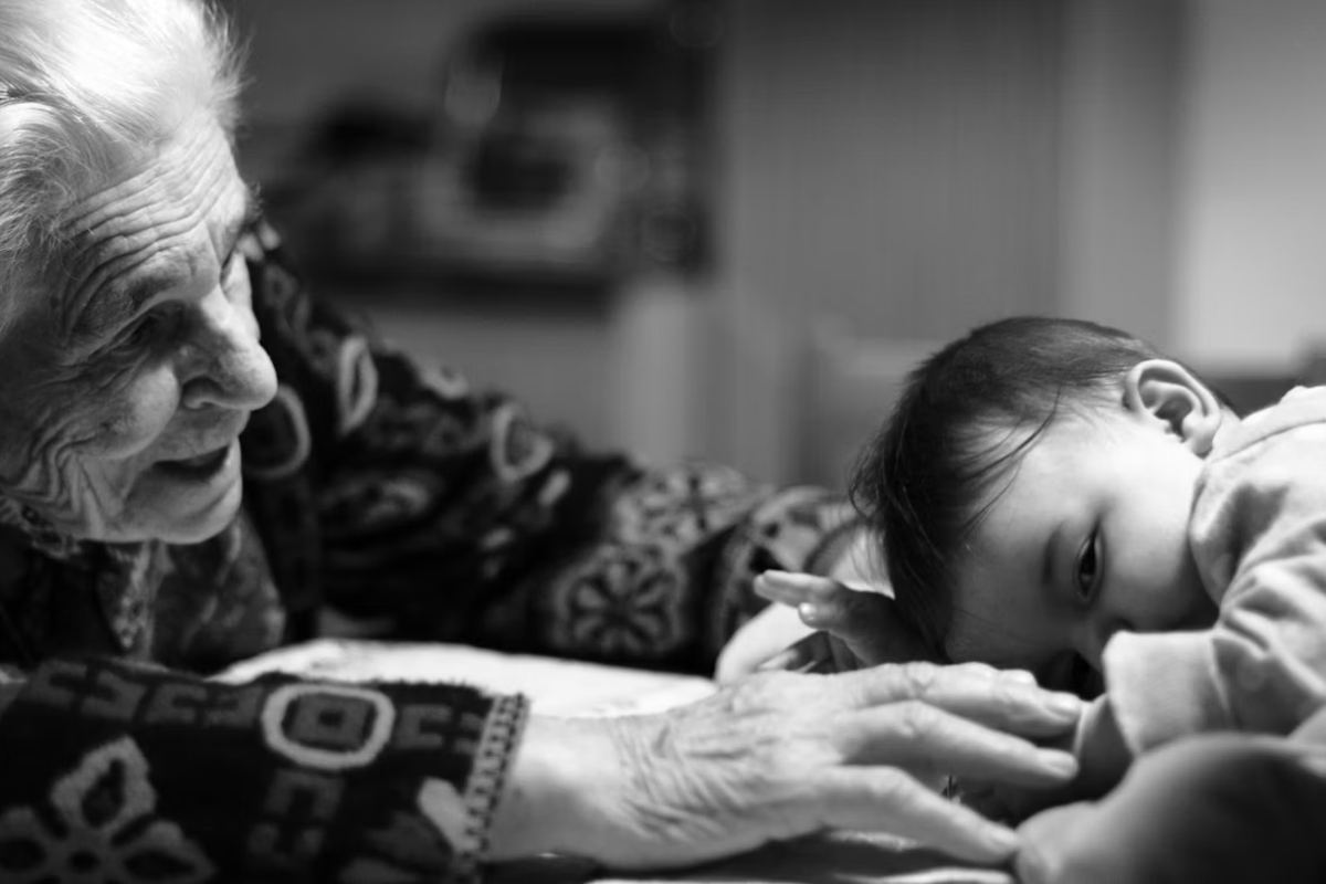 An older woman leaning over a baby lying on a bed