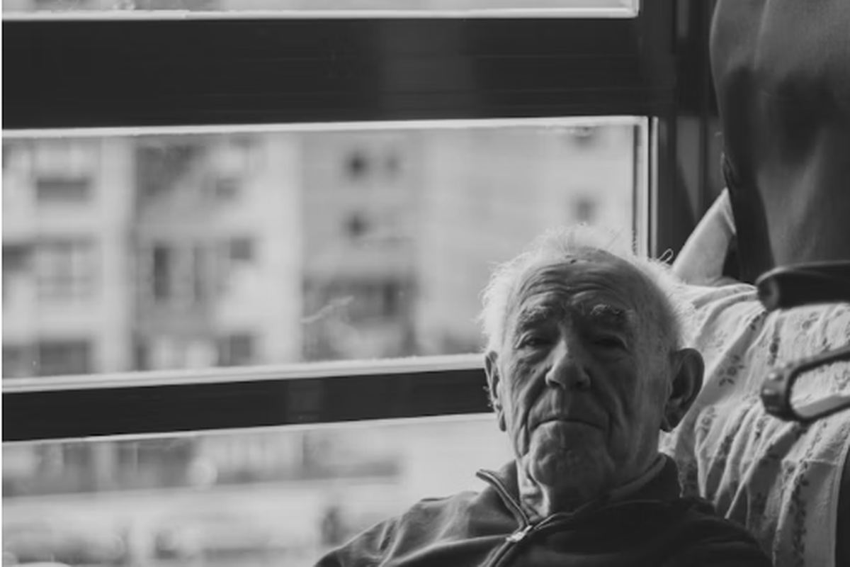 An older man sitting in an armchair beside a window in daylight