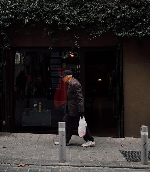 An older man walking past a shop with a shopping bag
