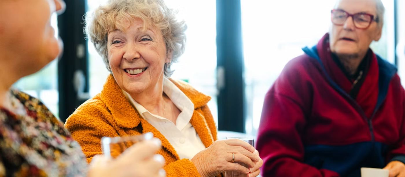 Three older adults sitting together with drinks, mid-conversation