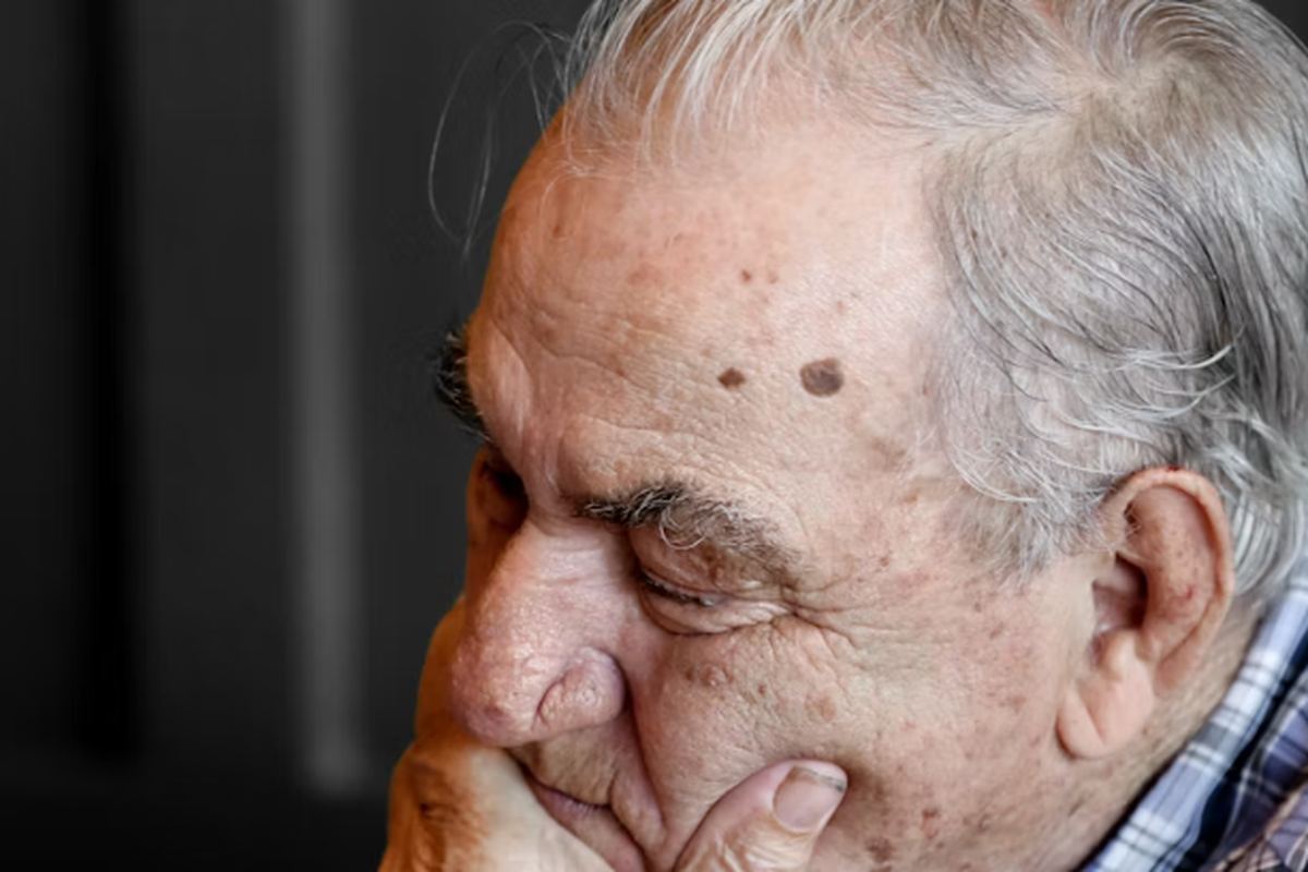 An older man resting his chin on his hand, eyes closed