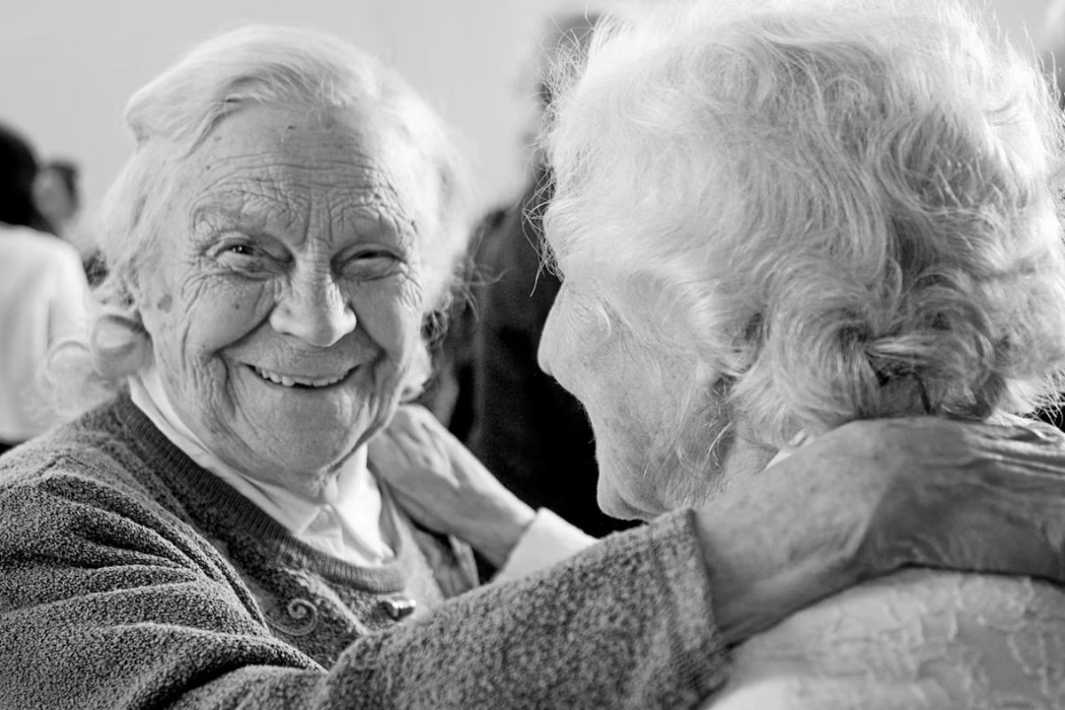Two older women greeting each other with an embrace