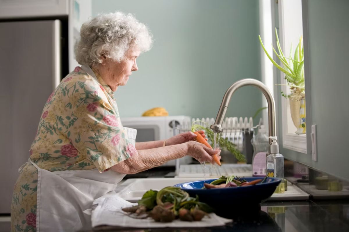 An older woman washing carrots and vegetables at a kitchen sink