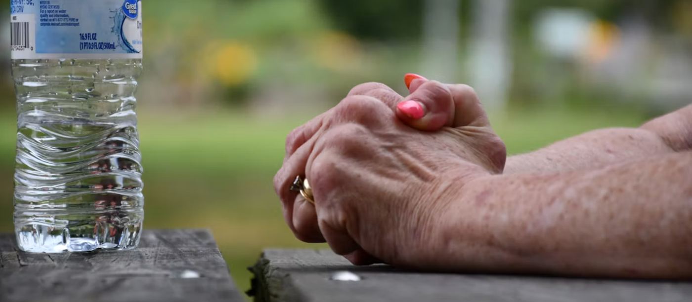 An older woman’s hands resting on a picnic table beside a bottle of water