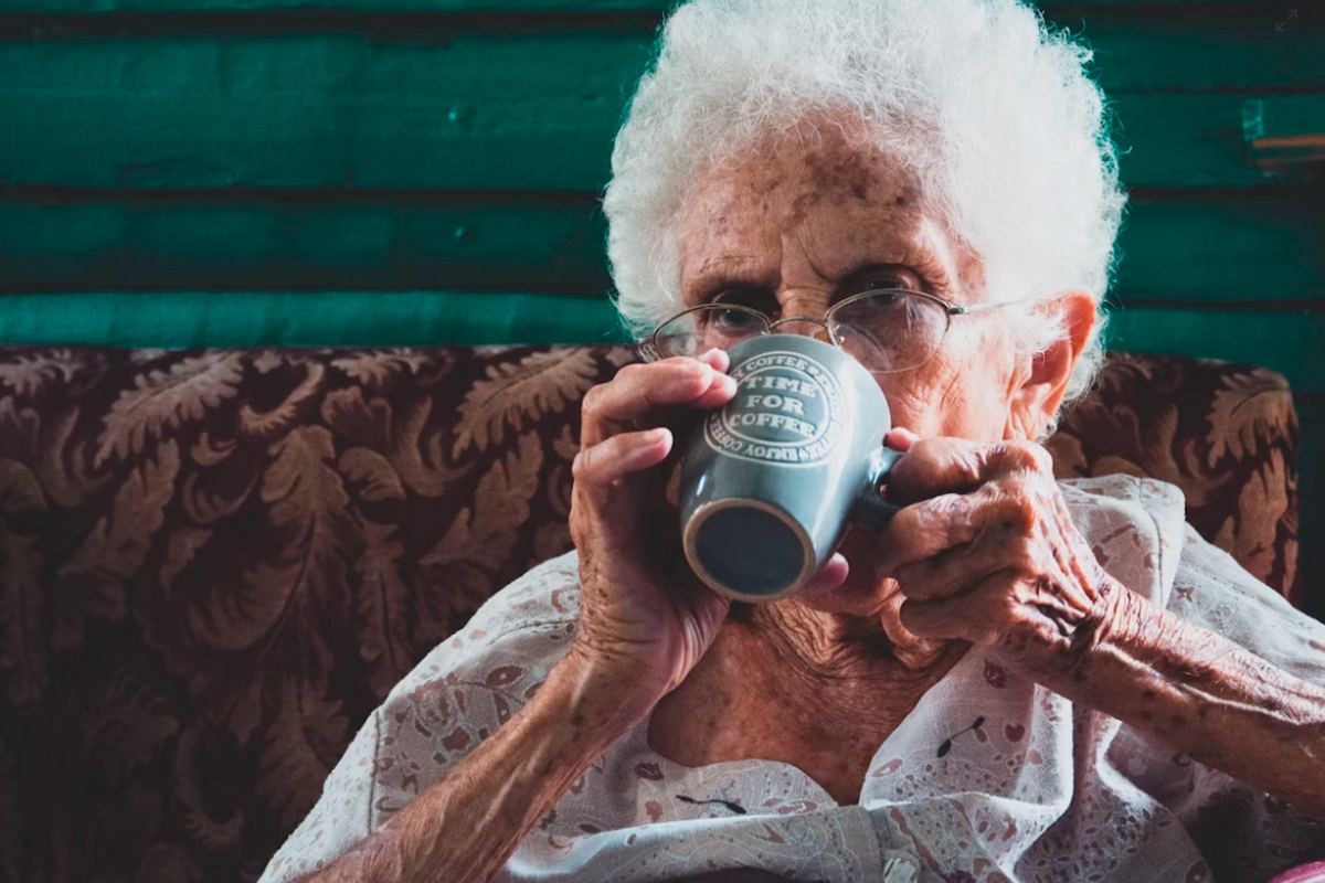An older woman drinking from a mug in an armchair